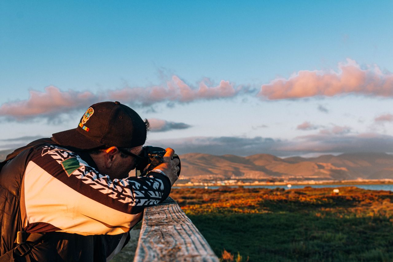 A man photographing a vast landscape during sunset, creating a vibrant and dynamic image.