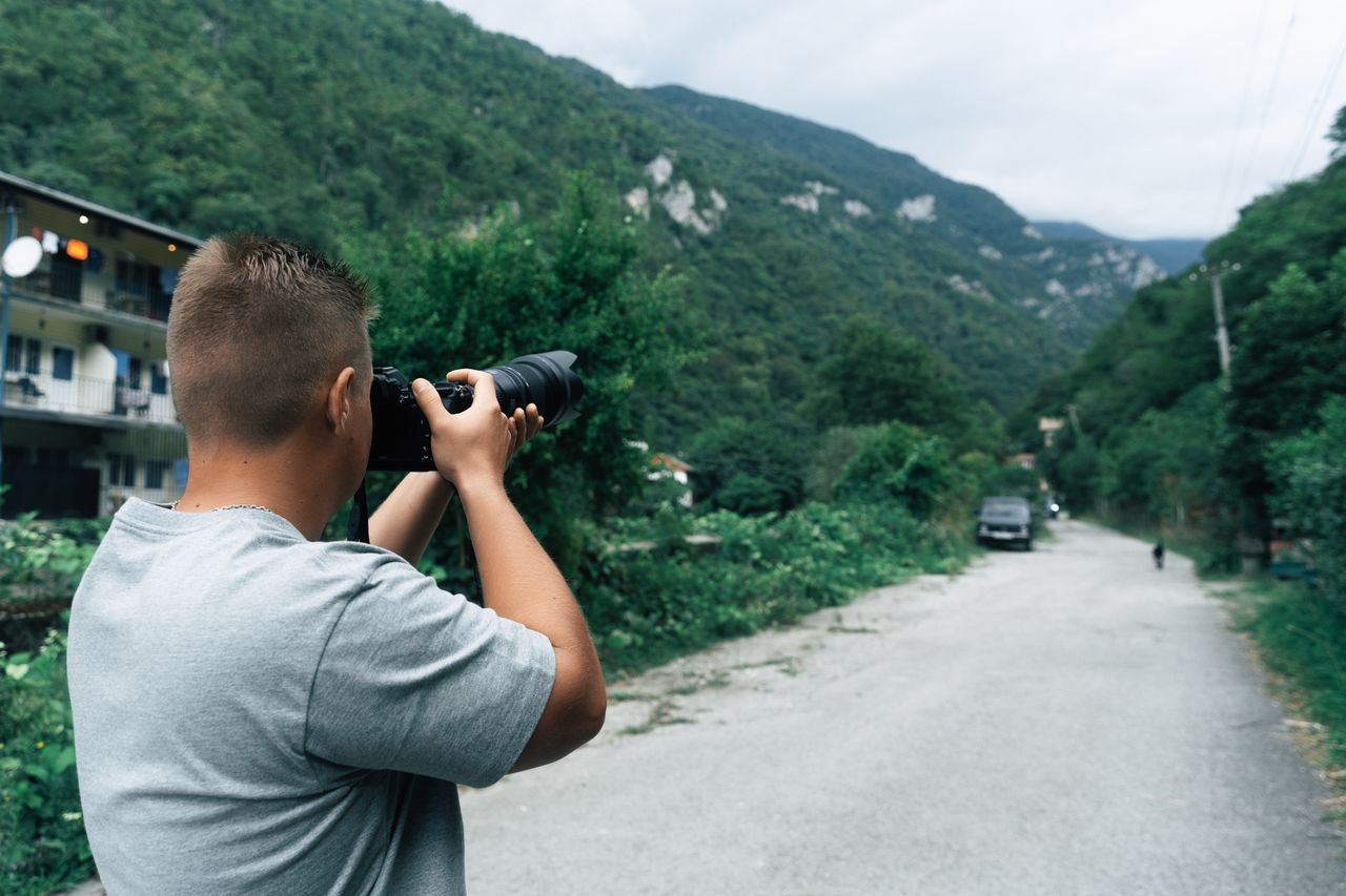 A man with a camera captures a scenic view in a mountainous area during daytime.