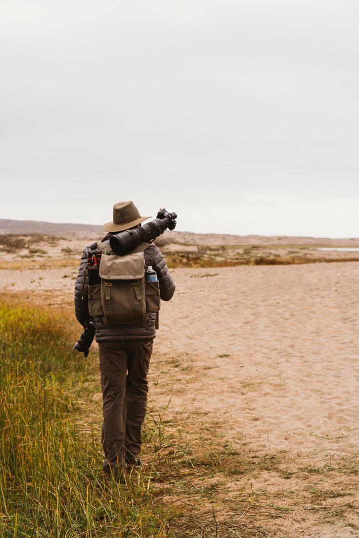 Person with camera gear walking along a beach path, showcasing a love for adventure and photography.